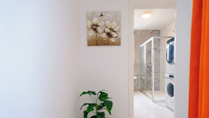 En hall med en krukväxt, en duschhörna och en tvättmaskin.
