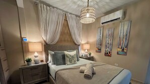 Ein Schlafzimmer mit Bett, Nachttischen, einer Lampe, einer Topfpflanze und Kunstwerken an den Wänden.