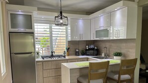 Eine moderne Küche mit integriertem Kühlschrank, Mikrowelle, Herd und Spüle. An der Kochinsel stehen Holzstühle und eine Hängeleuchte.