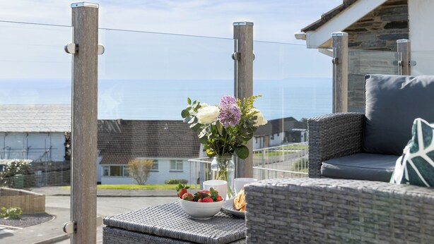 A balcony with wicker furniture, a bowl of strawberries, a vase with flowers, and a view of the sea. - Stylish coastal home with stunning sea views (Woolacombe)