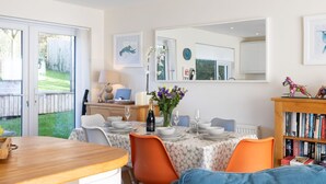 A dining area with a table set for four, a laptop on the table, and a bookshelf with books. - Stylish coastal home with stunning sea views (Woolacombe)