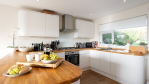 A modern kitchen with white cabinets, a wooden countertop, and a window providing a view of greenery outside. - Stylish coastal home with stunning sea views (Woolacombe)