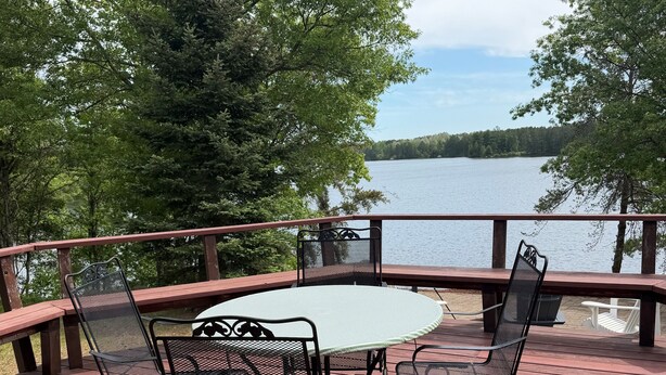A wooden deck with metal chairs and a table, overlooking a lake.