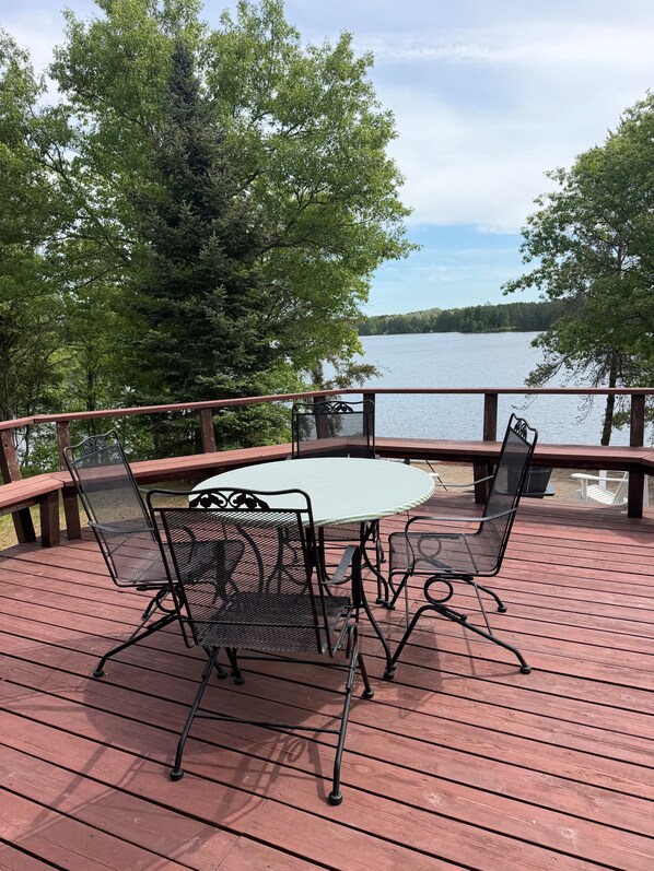 A wooden deck with metal chairs and a table, overlooking a lake.