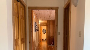 A wooden hallway with a wooden ceiling, a mirror on the wall, and a door at the end.