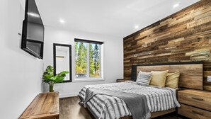 A modern bedroom with a wooden headboard, a large window, and a bedside table.