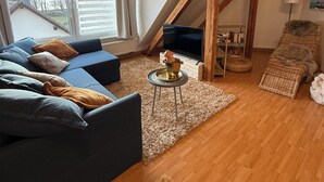 Un acogedor salón tipo loft con vigas de madera a la vista, un sofá azul, un televisor y un banco de mimbre.