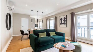 Ein modernes Wohnzimmer mit einem grünen Sofa, einem runden Couchtisch und einem Essbereich mit Tisch und Stühlen.