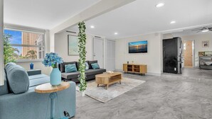 A modern living room with a grey sofa, a coffee table, and a TV. - Santorini Blu | Spacious 2BR Beachfront Suite (Hollywood)