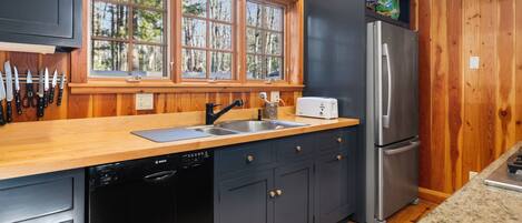 Una cocina con paredes de madera, un refrigerador de acero inoxidable, un lavavajillas Bosch y un ventanal con vistas a árboles.