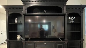 A dark wood entertainment center with a flat-screen TV, built-in shelves, and cabinets.