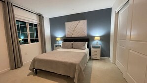 A bedroom with a bed, two bedside tables with lamps, a window with curtains, and a door.