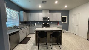 A modern kitchen with grey cabinets, a central island with two bar stools, a built-in microwave, and a gas stove.