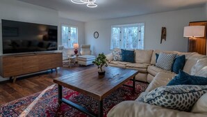 Een moderne woonkamer met een grote flatscreen-tv, een houten salontafel, een beige bank en een rood geweven vloerkleed.