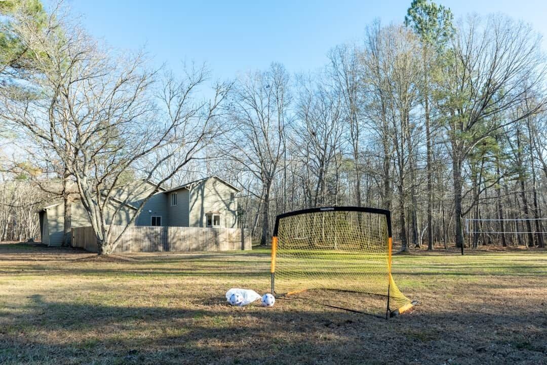 A soccer goal in a yard with a house and trees in the background.