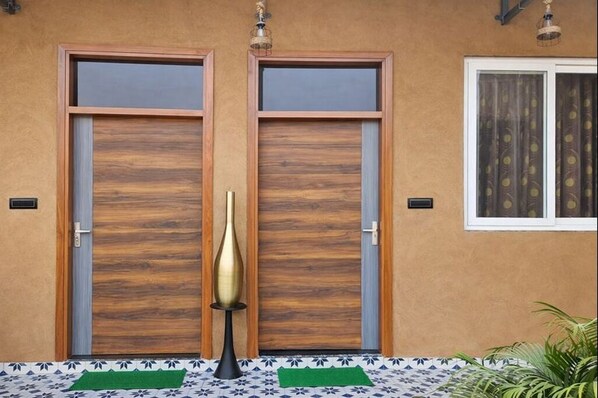 A building facade with two wooden doors, a decorative column, and a window with curtains.