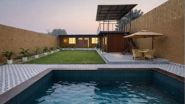 Ein Schwimmbecken mit gefliestem Beckenrand, einer Rasenfläche und einer Holzterrasse mit Gartenmöbeln.