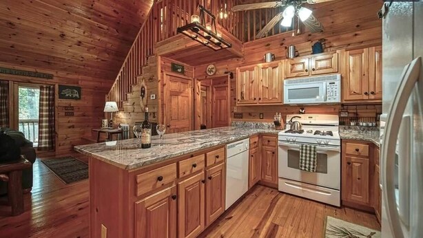 A wooden cabin interior with a kitchen featuring wooden cabinets, a granite countertop, a stove, a microwave, and a refrigerator.