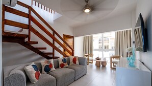 Ein modernes Wohnzimmer mit grauem Sofa, Holztreppe und einem großen Fenster mit Blick nach draußen.