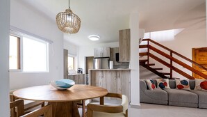Eine moderne Küche mit Holzausbau, ein Essbereich mit rundem Tisch und Stühlen sowie eine Treppe zu einem Wohnbereich mit einer Couch und bunten Kissen.