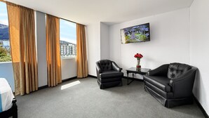 A hotel room with a large window, two black leather armchairs, a small table with a vase of red roses, and a flat-screen TV mounted on the wall. - HOTEL SANTA MARIA BY LAUZA (Quito)