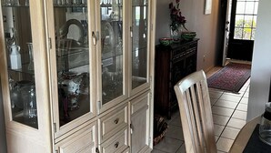 Ein Essbereich mit einem Holzschrank, der Gläser und eine Vase mit Blumen beherbergt.