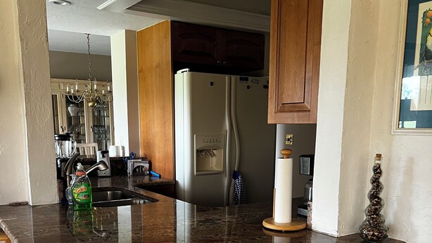 Eine Küche mit Granit-Arbeitsplatte, einem Kühlschrank, Holzschränken und einem Korbwäschesessel.