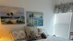 Ein Schlafzimmer mit einem großen Bett, mehreren Kissen, einem Nachttisch und einem Fenster mit Jalousien.