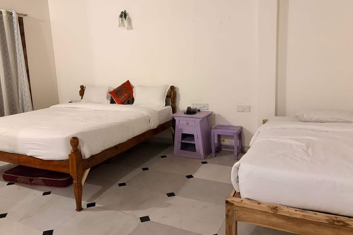 A room with two wooden beds, a small purple nightstand, and a white wall.