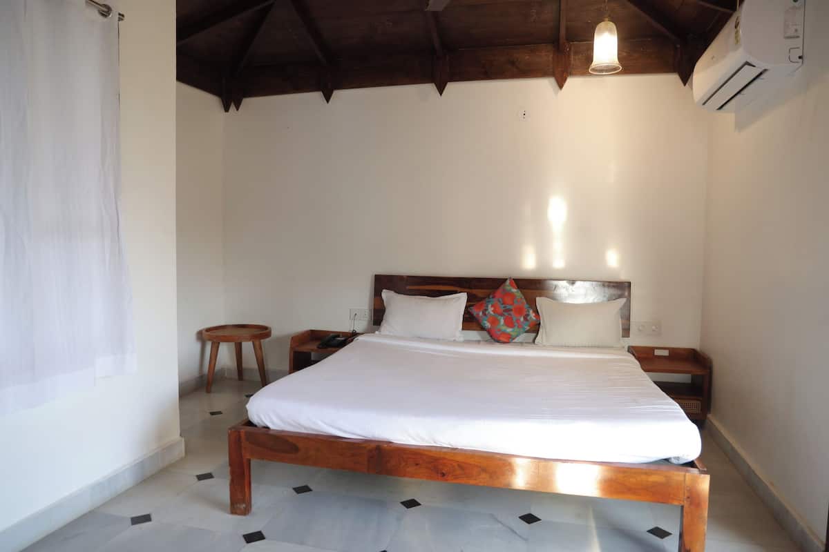 A bedroom with a wooden bed, white bedding, a small round stool, and a nightstand.