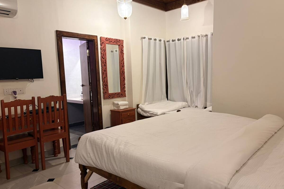 A bedroom with a large bed, a wooden chair, a bedside table, a mirror, and a television mounted on the wall.