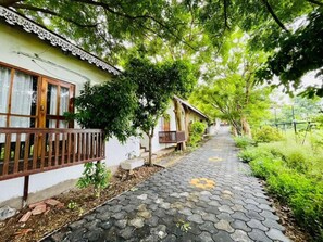 A pathway lined with traditional-style buildings, a paved walkway, and lush greenery. - Malgudi Days and Resorts (Ujjain)