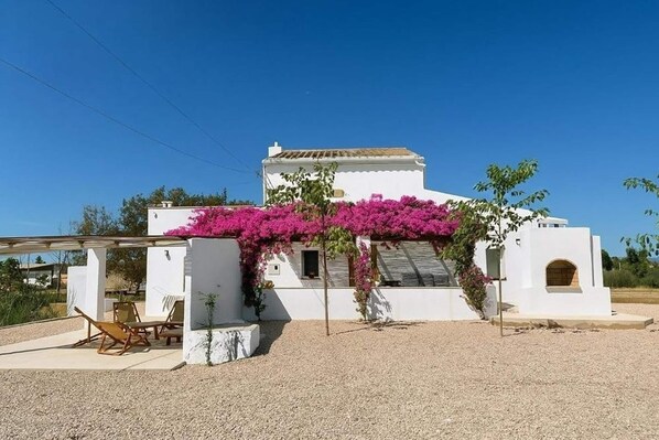 A white building with a pergola covered in pink flowers, a patio with chairs, and a gravel ground. - Mas Mido Century-old Farmhouse in Deltebre (Sant Jaume d'Enveja)