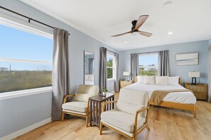 A bedroom with a large bed, two chairs, a desk, a ceiling fan, and a view of the outdoors. - Good Vibrations - Steps to the Beach! (St. Augustine)