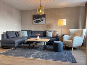 A modern living room with a sectional sofa, a coffee table, a floor lamp, and a large painting on the wall.