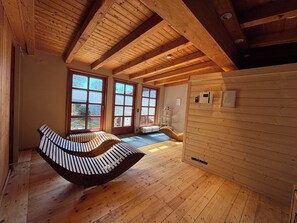 A wooden interior with a curved bench, large windows, and a wooden wall with a mounted device.