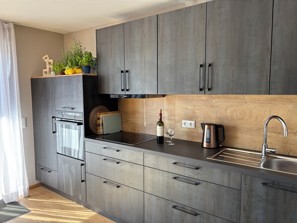 A modern kitchen with grey cabinets, a built-in oven, a sink, and a wine bottle.