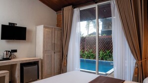 A hotel room with a bed, a desk with a television, a small kitchenette, and a view of a swimming pool. - Sunsei Beach Negombo (Negombo)