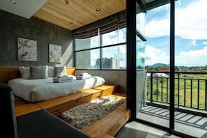 A bedroom with a large bed, a view of the city, and a balcony.