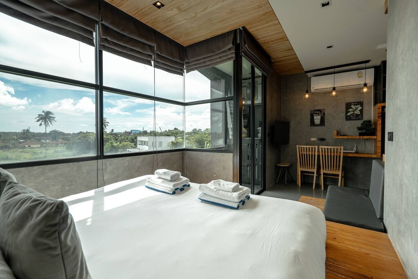 A modern hotel room with a large bed, a dining area, and a view of the landscape.