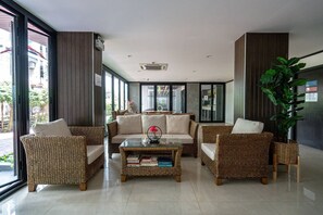 A modern lounge area with wicker furniture, a glass coffee table, and large windows offering a view of the street.