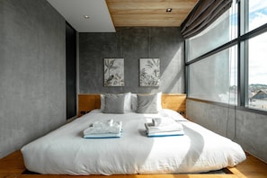 A modern bedroom with a large bed, wooden headboard, grey walls, and artwork.