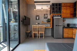 A modern kitchen with a built-in refrigerator, wooden cabinets, a dining area with a table and chairs, and a large window overlooking a balcony.