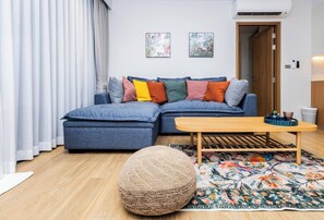 A living room with a sectional sofa, a round pouf, a wooden coffee table, and a patterned rug. - Suite Azure 2br | Laguna beachside bang tao beach (Choeng Thale)