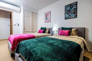 A hotel room with two beds, each with a different colored bedspread, a nightstand with a lamp, and two framed pictures on the wall. - Suite Azure 2br | Laguna beachside bang tao beach (Choeng Thale)