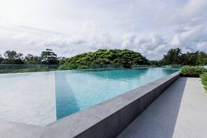 A swimming pool with a clear blue water surface, surrounded by a low stone wall and lush greenery. - Suite Azure 2br | Laguna beachside bang tao beach (Choeng Thale)