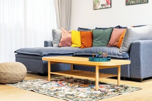 A modern living room with a grey sofa, colorful cushions, a wooden coffee table, and a floral rug. - Suite Azure 2br | Laguna beachside bang tao beach (Choeng Thale)