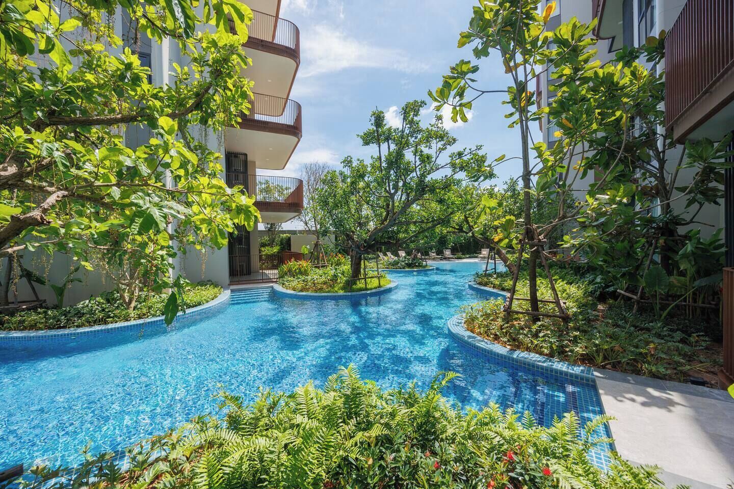 A pool area with a curved design, surrounded by lush greenery and modern buildings.