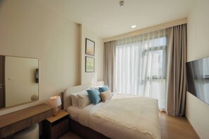 Quarto de hotel com cama, mesa de cabeceira, abajur, televisão e uma janela grande com cortinas.