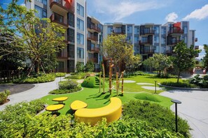 A modern residential complex with multiple balconies, a landscaped garden with green lawns, and yellow circular seating areas. - Suite Eden 2br|garden & Pool|canvas bang tao beach (Choeng Thale)